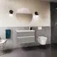 Waschtisch mit modernem Design, montiert an der Wand, in Holzoptik. Ideal Standard Armatur und runder Spiegel sowie handtuchhalter sind sichtbar. Badezimmer-Umgebung.